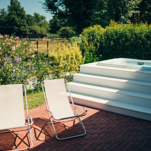 Two lounge chairs and a jacuzzi in a garden with flowers.