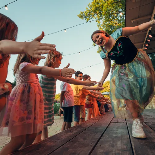Children and adults high-fiving on a wooden stage at sunset.