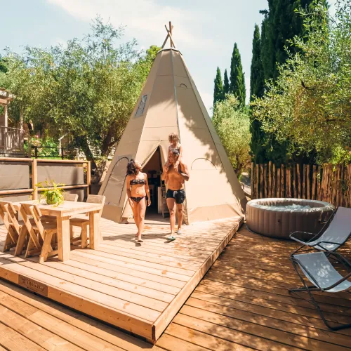 Couple walking from a teepee on a sunny deck with trees around.