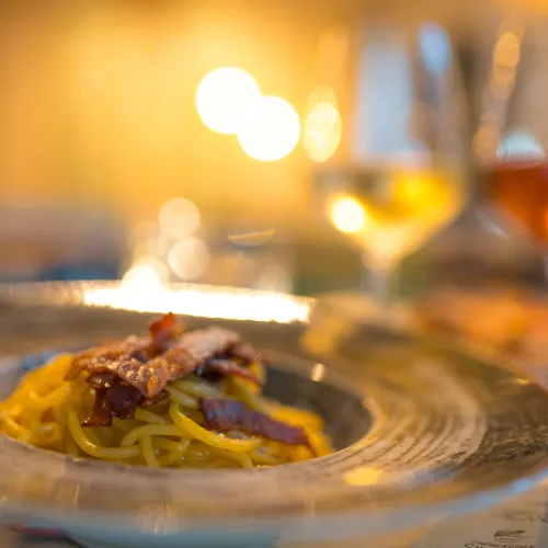 Pasta dish on a plate with two glasses of wine in a warm, softly lit setting.