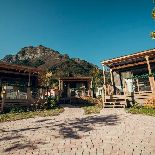 Cabins with wooden porches, mountain backdrop, clear sky.