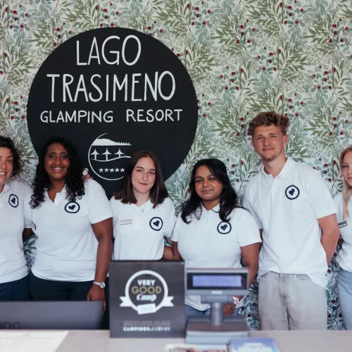 Staff in white shirts at a resort reception desk, smiling.