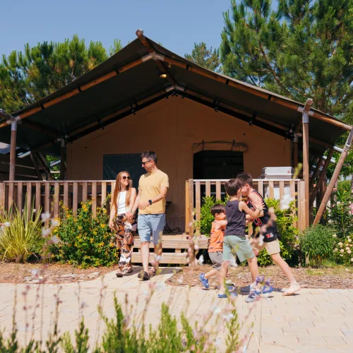 Family walking near a cabin with trees and flowers.