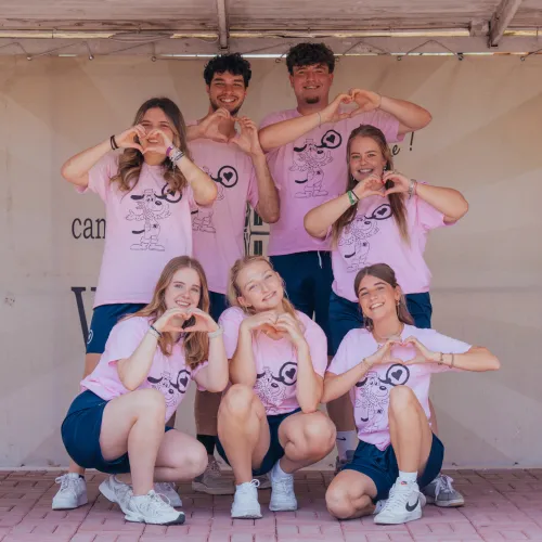 Group of people wearing pink shirts and shorts, posing with hand hearts.