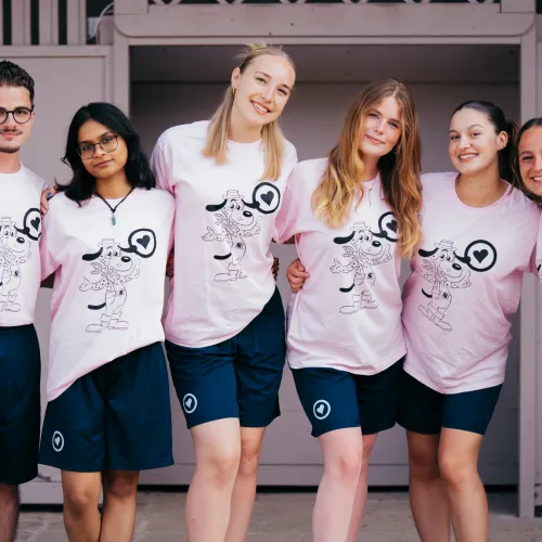 A group of five people wearing matching pink shirts and blue shorts, smiling together.