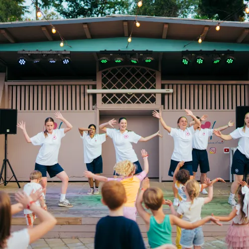 Children dance along with performers on an outdoor stage.