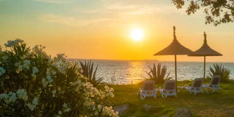 Tropical sunset over the lake with lounge chairs and parasols on the grassy shore.