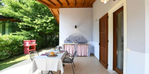Covered patio with table, chairs, and outdoor kitchen surrounded by greenery.