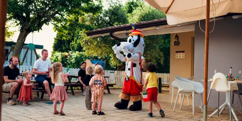 Kids smiling at a costumed character outside under a sunny patio.