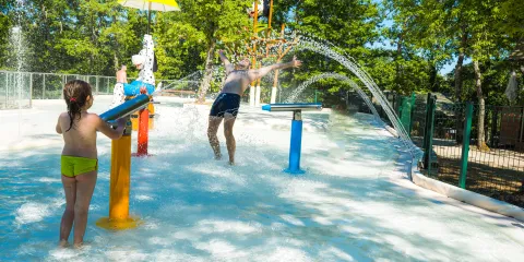 Children playing in a colorful water park with fountains and trees.