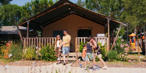 Family walking near a cabin with trees and flowers.