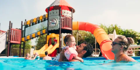 Family enjoying a sunny day at a pool with colorful slides in the background.