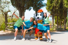Four people posing with a Dalmatian character in a park on a sunny day.