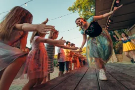 People dancing and reaching hands under string lights at an outdoor event.