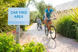 Cyclists riding on a path in a car-free area, surrounded by greenery.