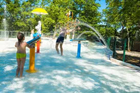 Children playing in a colorful water park with fountains and trees.