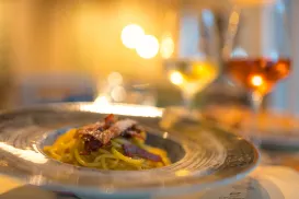 Pasta dish on a plate with two glasses of wine in a warm, softly lit setting.