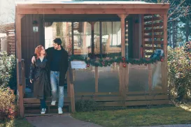 Couple smiling outside a wooden building decorated with garlands.