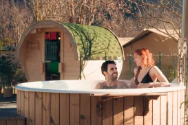 Outdoor hot tub with two people, wooden cabin in background.