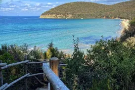 Wooden path leading to a turquoise bay with hills in the distance.