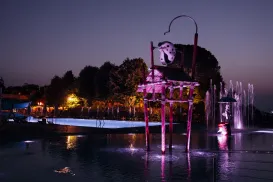 Fountain at night with purple lighting and water jets, trees silhouetted in the background.
