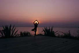 Yoga pose by a lake at sunset, silhouette against a purple sky.