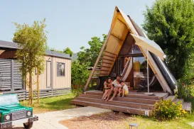 A-frame cabin with people sitting on the steps, surrounded by greenery.