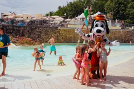 Children in swimsuits enjoy a water park with a costumed character.