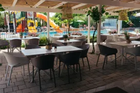 Poolside patio with tables and chairs, colorful play slide in the background.