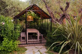Wooden garden gazebo with a table, surrounded by lush greenery.