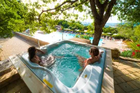 People relaxing in a hot tub overlooking a bright, sunny pool area.