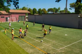 Kids playing soccer on a sunny day in a fenced field.