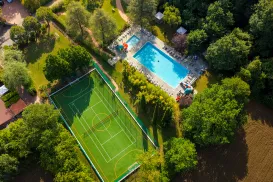 Tennis court and pool surrounded by trees, aerial view.