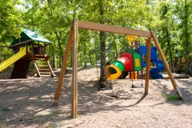 Playground with swings, a slide, and colorful climbing structure in a wooded area.