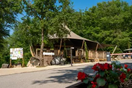 Rustic wooden building with a canopy surrounded by trees and flowers.