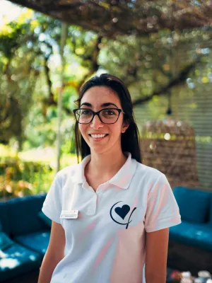 Young woman smiling in a sunny outdoor setting, wearing glasses and a polo shirt.