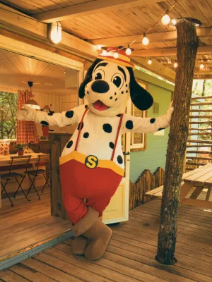 spotty in red shorts at a cozy wooden cabin entrance.