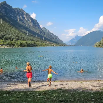 Children playing by a mountain lake under a clear blue sky.