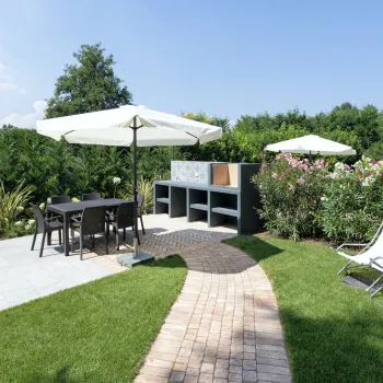 Sunny garden with patio furniture, umbrellas, deck chairs, and lush greenery.