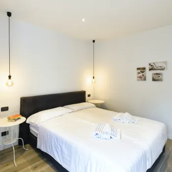 Minimalist bedroom with white walls and bed, two hanging lights, and side tables.