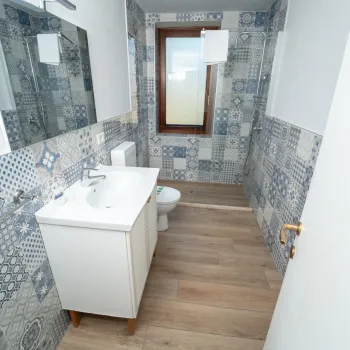 Narrow bathroom with patterned tiles, wooden floor, and a window.