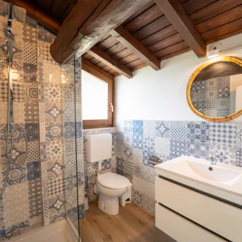 Rustic bathroom with patterned tiles, round mirror, and wooden ceiling beams.