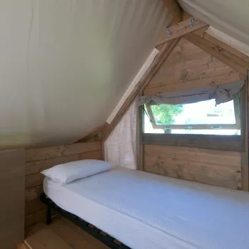 Single bed in a small wooden cabin with a window and soft light.