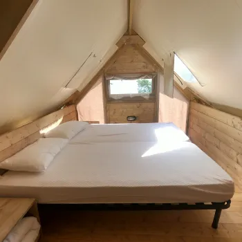 Cozy wooden attic bedroom with a white double bed and sunlight streaming through a small window.