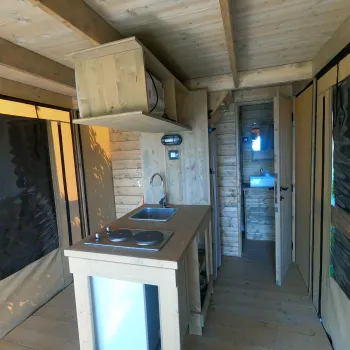Wooden cabin kitchen with stove, sink, and narrow walkway.