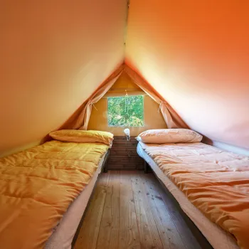 Two sleeping bags inside an orange tent with a view of trees outside.