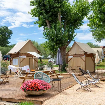 Outdoor glamping site with tents, deck chairs, and trees under a blue sky.