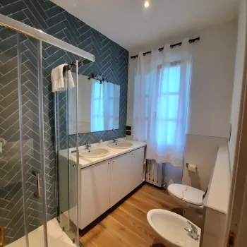 Modern bathroom with glass shower, dual sinks, and white fixtures.