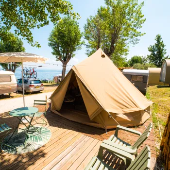 Canvas tent on wooden deck, surrounded by trees, with caravans nearby.