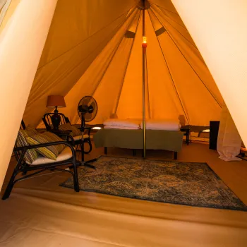 Luxurious tent interior with bed, chairs, and rug. Warm lighting.
